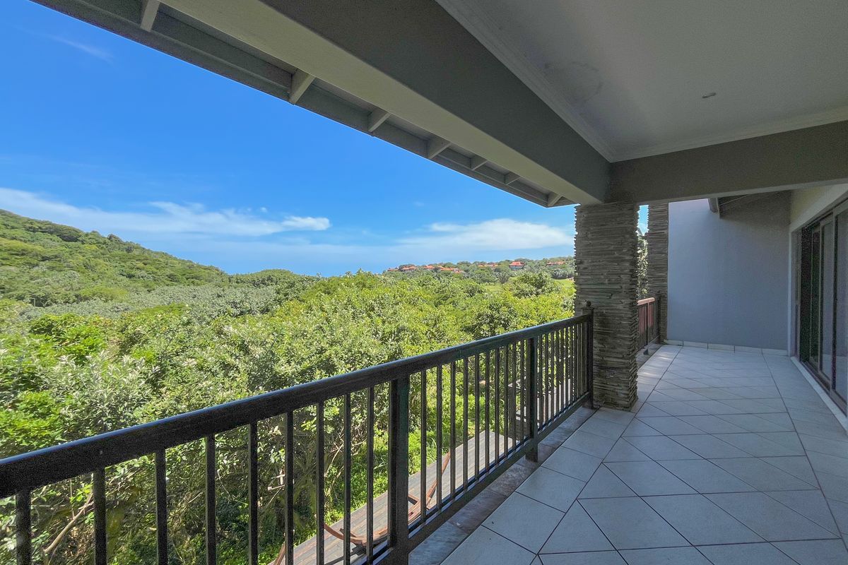 A spacious covered balcony featuring tiled flooring, a stone-clad pillar, and a metal balustrade, offering expansive views of the surrounding natural landscape.