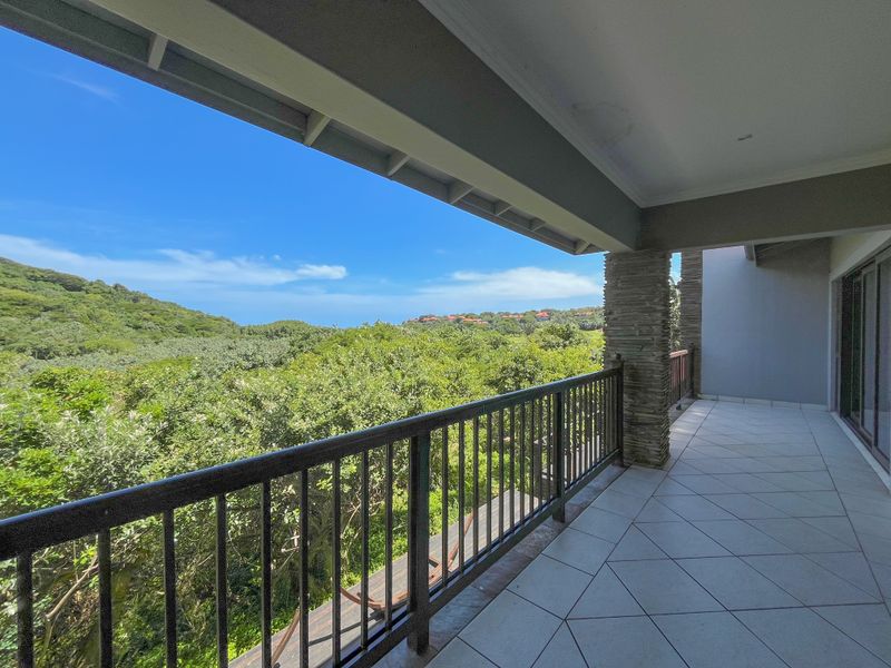 A spacious covered balcony featuring tiled flooring, a stone-clad pillar, and a metal balustrade, offering expansive views of the surrounding natural landscape.