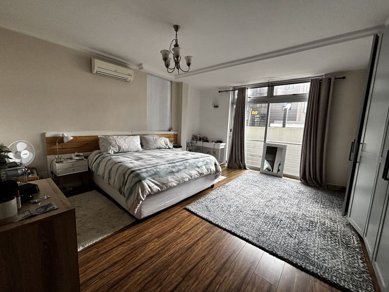 Spacious bedroom featuring wood-look flooring, a wall-mounted air conditioning unit, and large sliding glass doors providing access to a balcony.