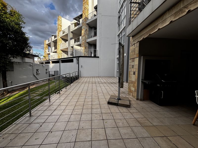 Spacious tiled balcony featuring a built-in braai area, stainless steel railings, and views of the apartment complex facade.