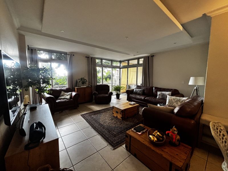 Spacious living room featuring large windows, tiled flooring, and a recessed ceiling design, offering ample natural light and access to an outdoor area.