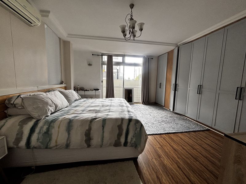 Spacious bedroom featuring extensive built-in cabinetry, wood-look flooring, a wall-mounted air conditioning unit, and direct access to a private balcony.