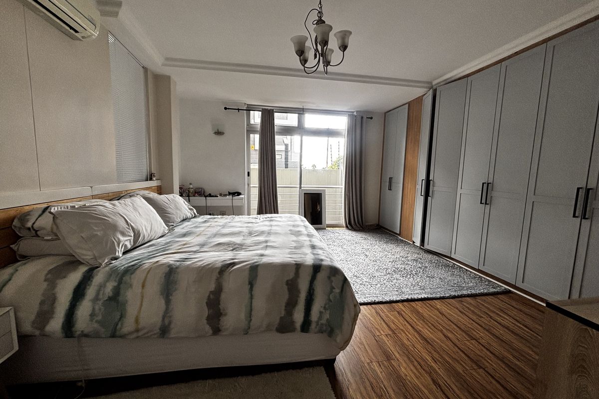 Spacious bedroom featuring extensive built-in cabinetry, wood-look flooring, a wall-mounted air conditioning unit, and direct access to a private balcony.