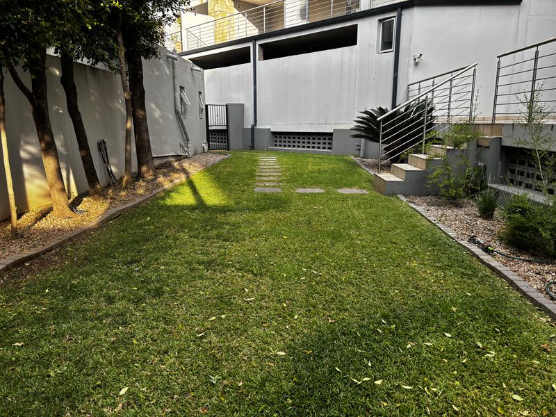A private rear garden area featuring a manicured lawn, stone stepping path, and a staircase leading to an elevated patio level.