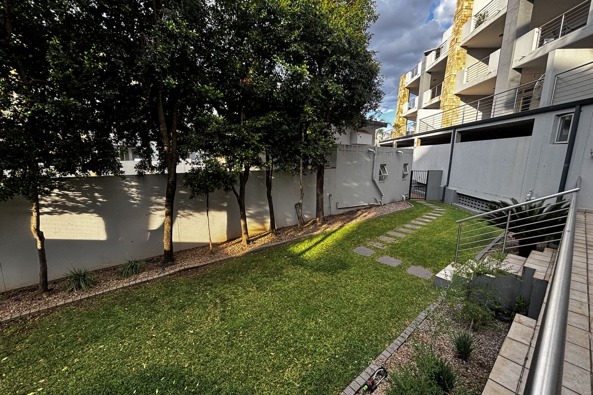 A well-maintained rear garden area featuring a manicured lawn, stone pathway, and perimeter walling, adjacent to the apartment building structure.