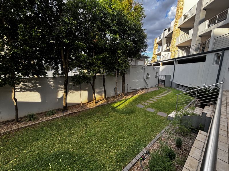 A well-maintained rear garden area featuring a manicured lawn, stone pathway, and perimeter walling, adjacent to the apartment building structure.