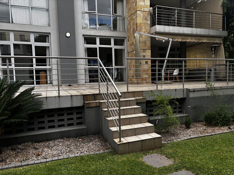Spacious elevated patio area featuring stainless steel railings, tiled flooring, and direct access to the garden through large glass sliding doors.