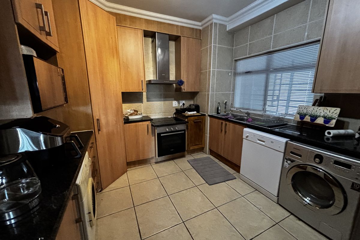 A functional kitchen featuring wood-finish cabinetry, granite countertops, a built-in oven with extractor fan, and tiled flooring with integrated appliance spaces.