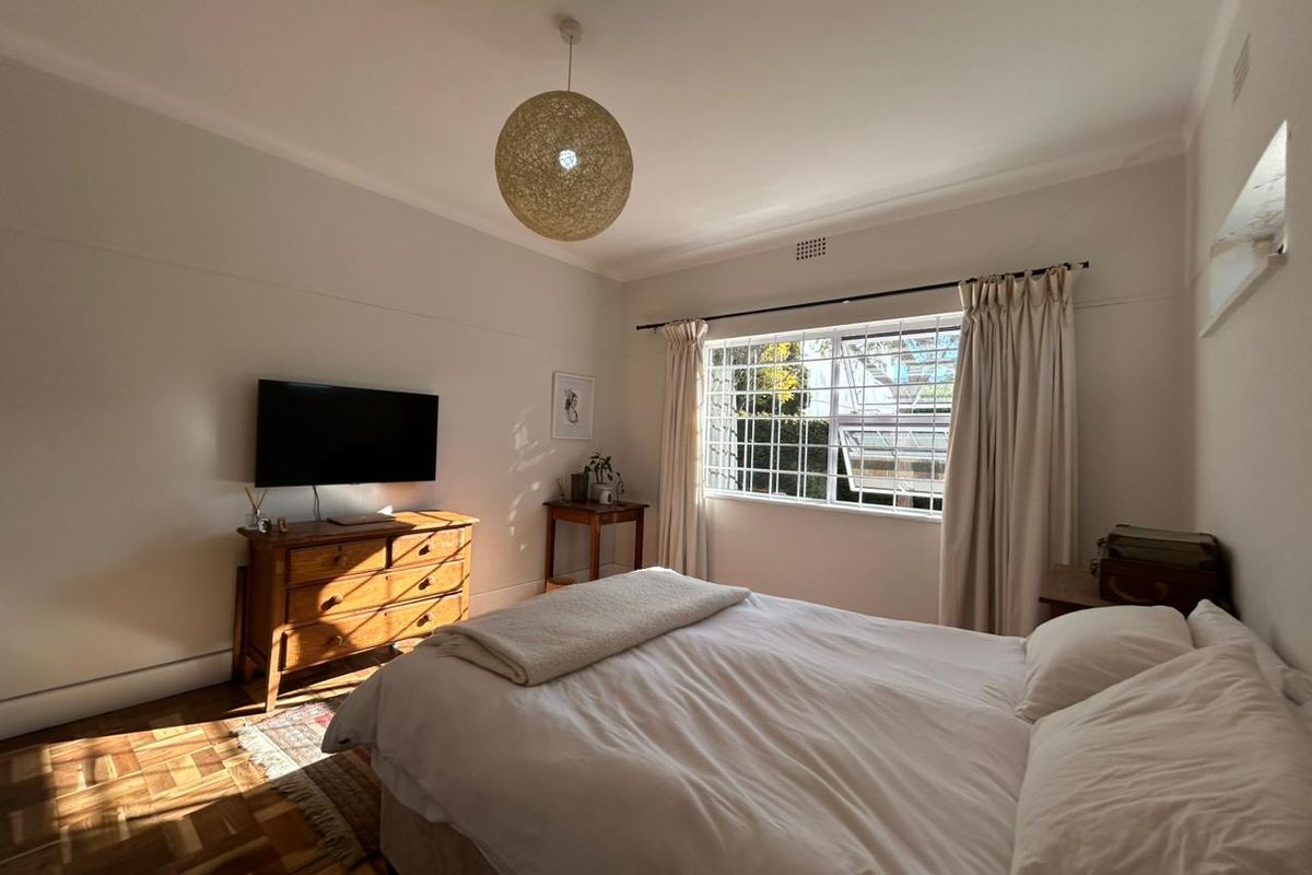 A well-lit bedroom featuring classic parquet flooring, a large window with security bars, and neutral wall finishes.