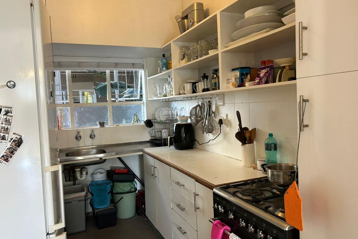 Compact kitchen featuring white cabinetry, open shelving, a stainless steel sink, and a gas stove, offering functional storage and preparation space.
