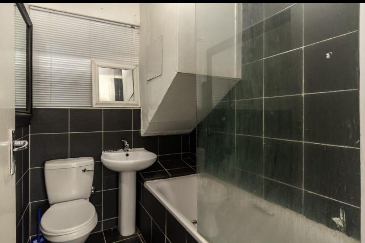 A compact bathroom featuring dark wall tiles, a pedestal basin, a toilet, and a bathtub with a glass shower screen.