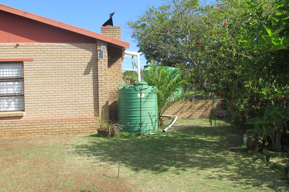 A view of the rear exterior of the house featuring a brick facade, a rainwater storage tank, and a garden area.