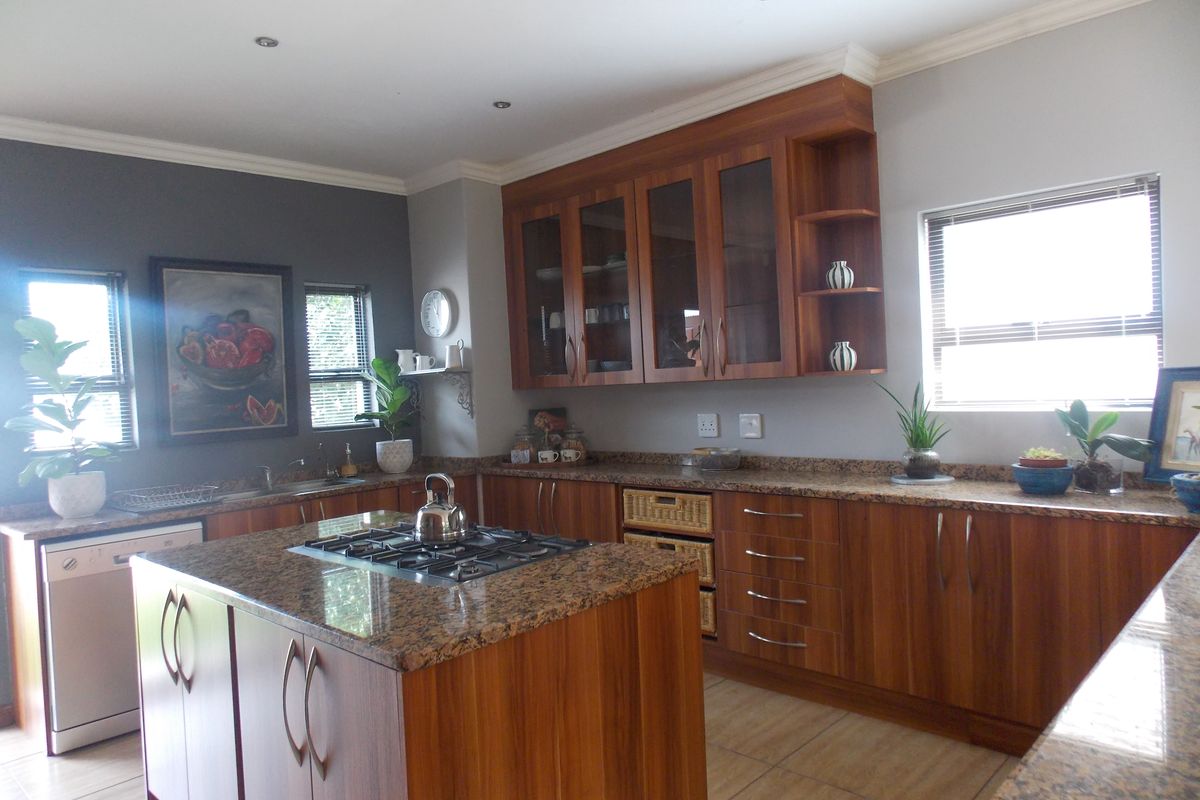 A well-appointed kitchen featuring wood-finish cabinetry, granite countertops, a central island with a built-in gas hob, and integrated dishwasher space.