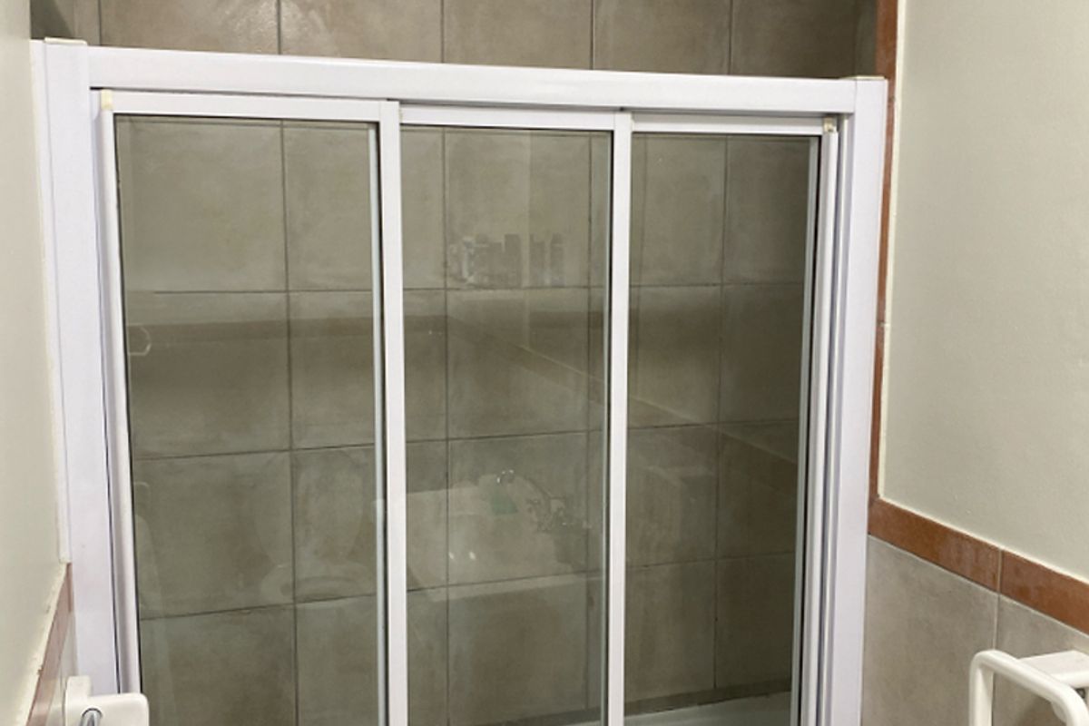 A bathroom featuring a built-in bathtub with a sliding glass shower screen and neutral-toned wall tiling.