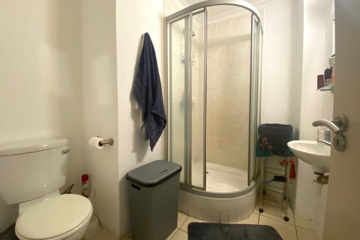 Compact bathroom featuring a corner shower enclosure, pedestal sink, and toilet with tiled flooring.