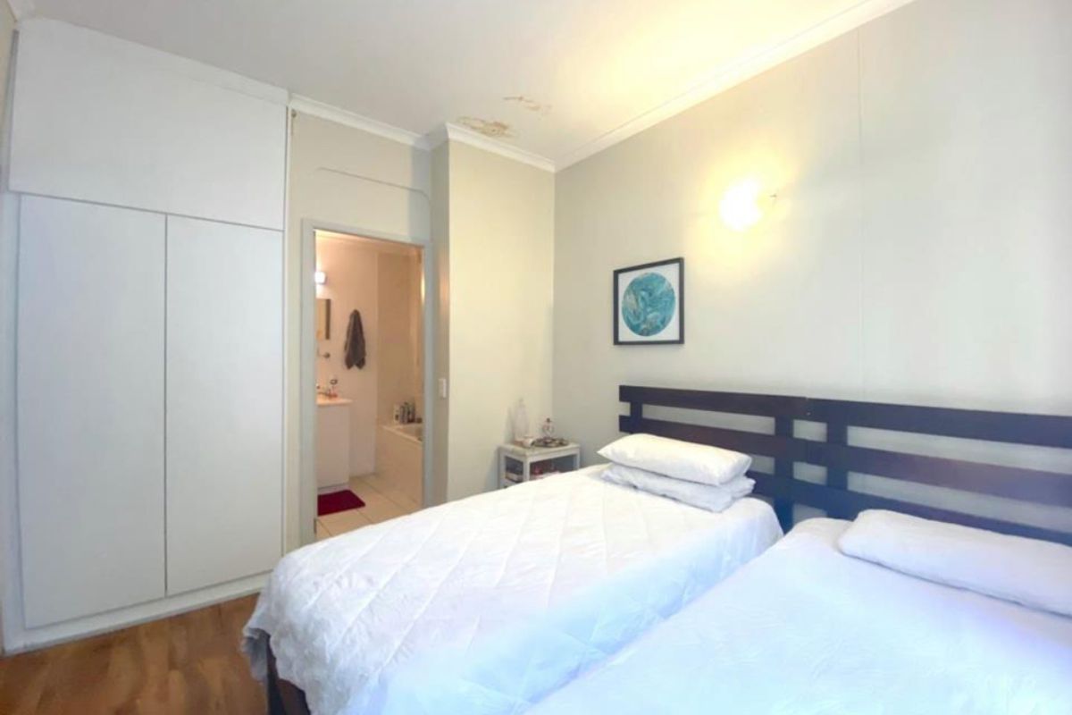 Bedroom featuring built-in cupboards, laminate flooring, and an en-suite bathroom. The ceiling shows visible signs of water damage.