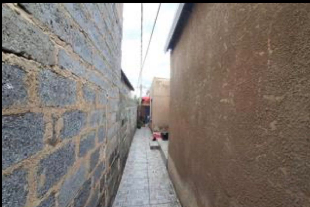 A narrow exterior side passage between two structures, featuring tiled flooring and exposed masonry walls.