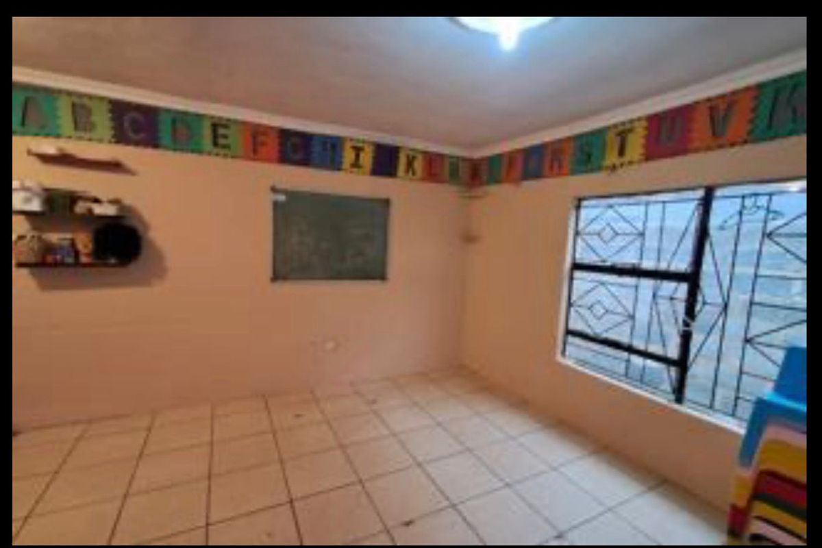 A functional bedroom space featuring tiled flooring, a large window with security bars, and neutral wall finishes, suitable for a child's room or study.