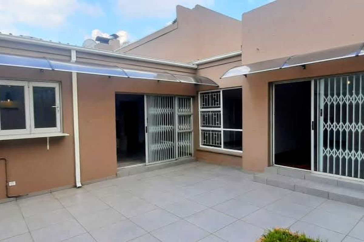 Rear exterior view featuring a tiled patio area, sliding glass doors with security gates, and protective polycarbonate awnings over the windows and doors.