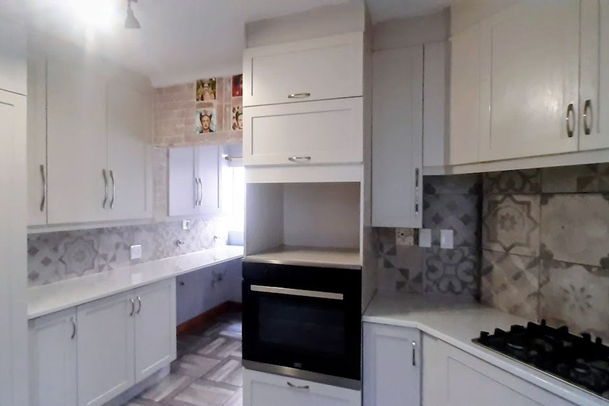 A clean, modern kitchen featuring white cabinetry, stone countertops, a built-in oven, and a gas hob with decorative patterned tile backsplash.