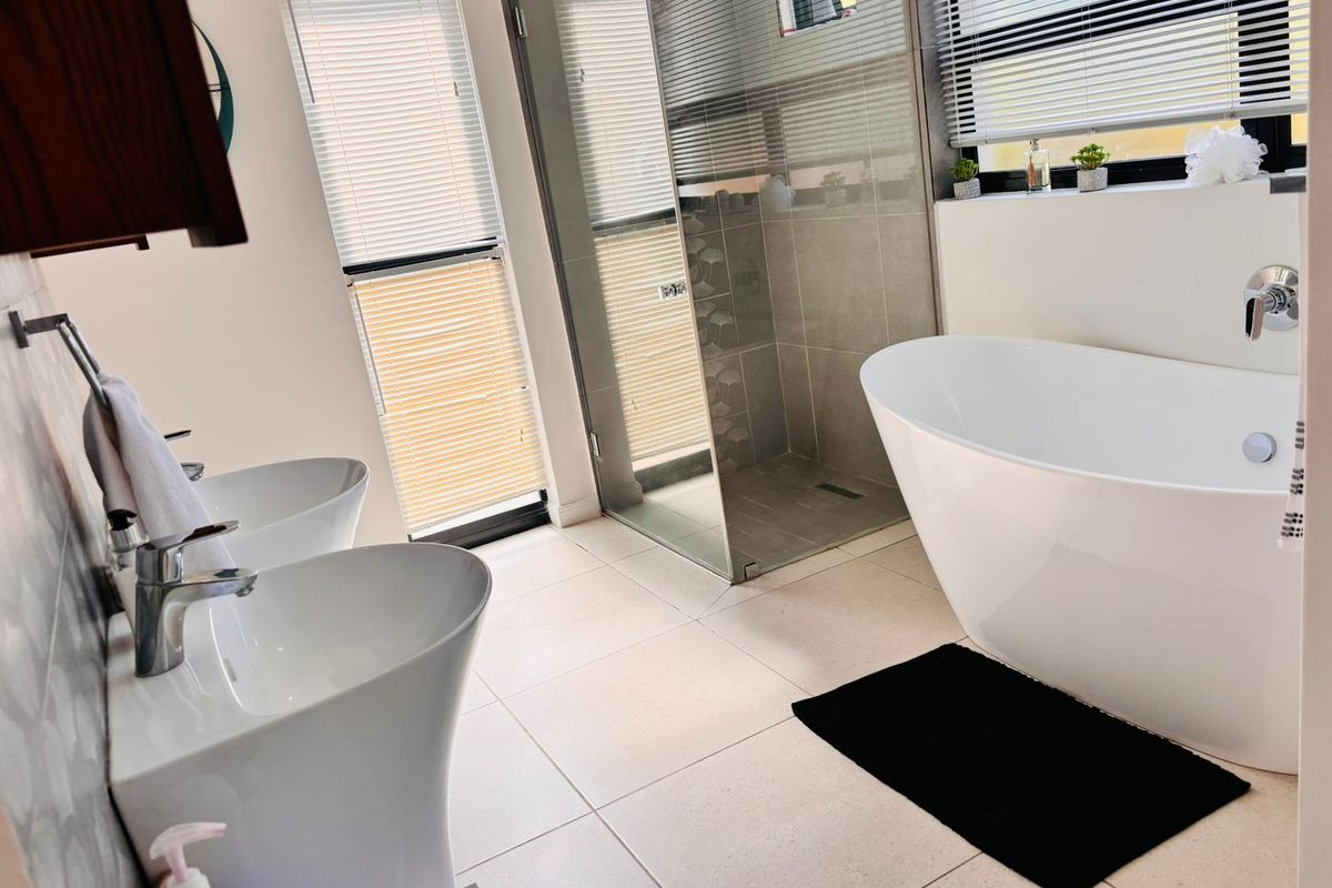 Modern bathroom featuring a sleek freestanding bathtub, a spacious walk-in shower, and dual pedestal sinks with contemporary chrome fixtures.