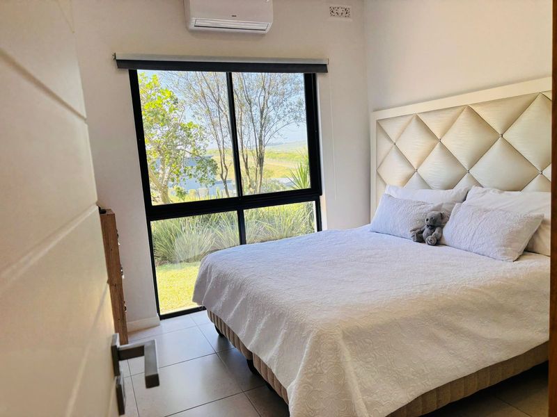 A bright bedroom featuring tiled flooring, a split-system air conditioner, and a large window with views of the garden.