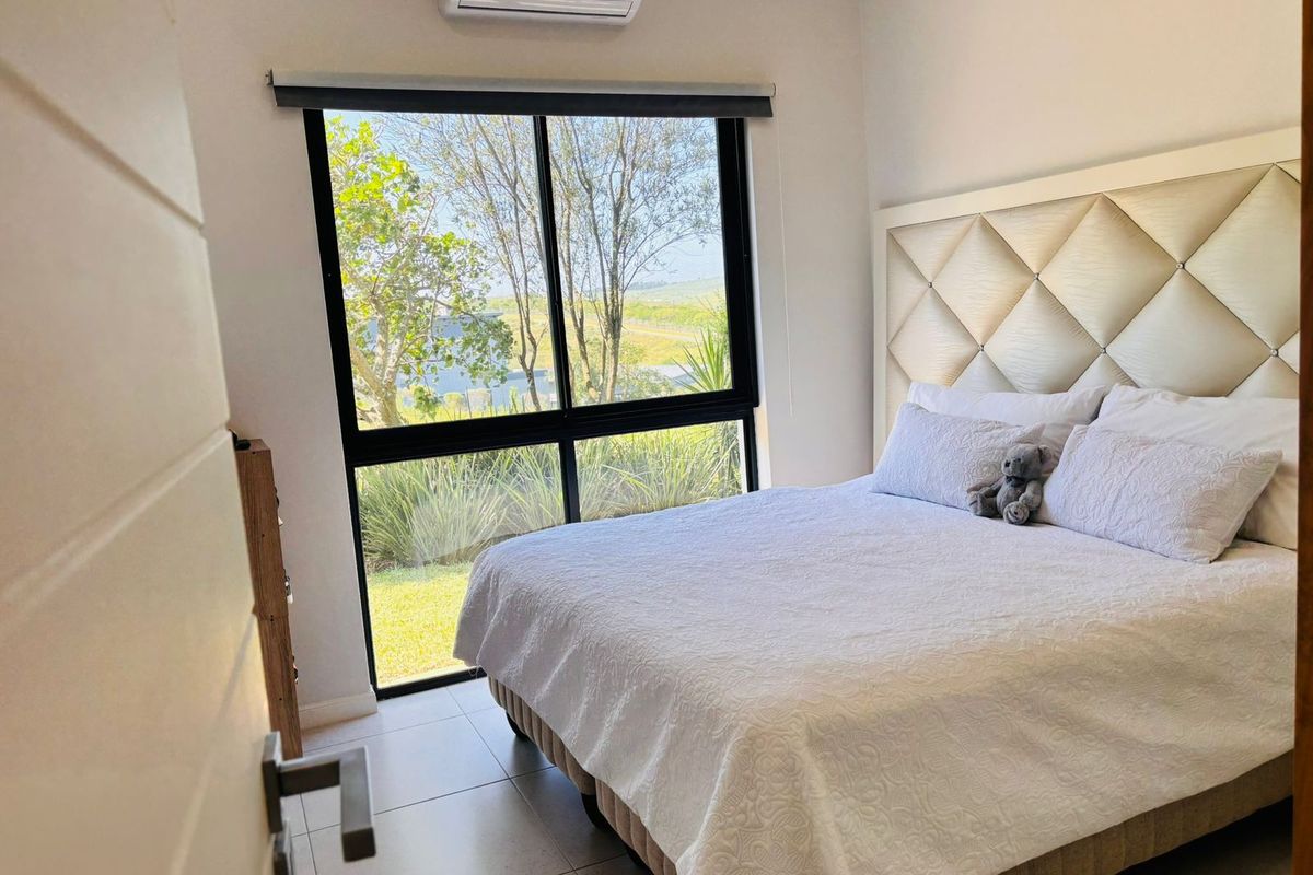 A bright bedroom featuring tiled flooring, a split-system air conditioner, and a large window with views of the garden.