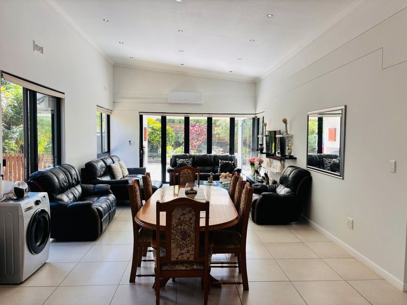 Spacious open-plan living and dining area featuring tiled floors, recessed lighting, and large stacker doors providing seamless access to the outdoor garden space.