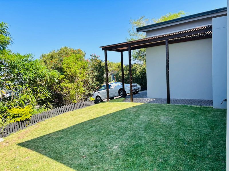 A well-maintained rear garden area featuring a modern pergola structure, paved driveway section, and established landscaping with a picket fence.