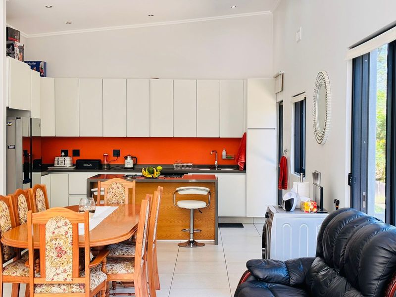 Open-plan kitchen and dining area featuring modern white cabinetry, a vibrant orange splashback, tiled flooring, and direct access to the outdoor space.