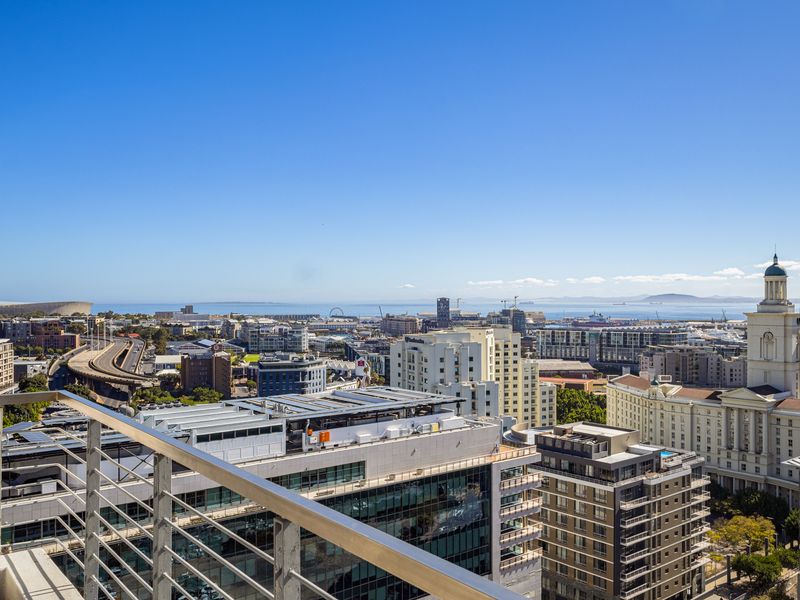 Elevated panoramic city and coastal view captured from a balcony with a modern metal railing.