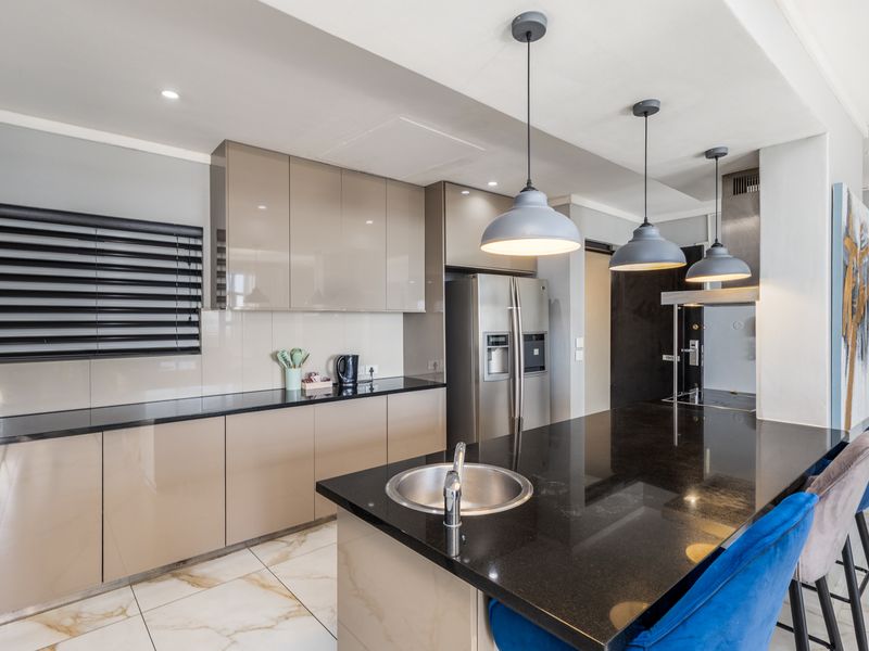 Modern kitchen featuring high-gloss cabinetry, sleek granite countertops, a central island with an integrated sink, and stylish pendant lighting.