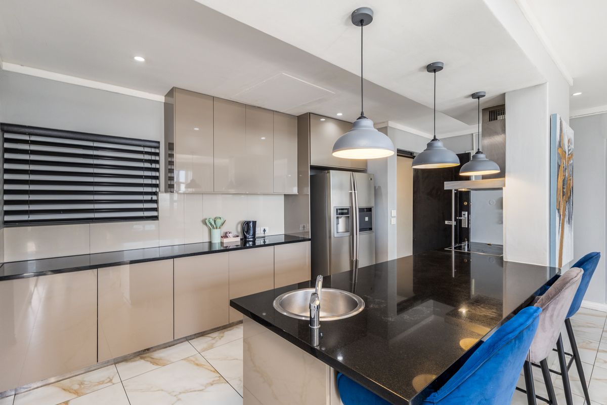 Modern kitchen featuring high-gloss cabinetry, sleek granite countertops, a central island with an integrated sink, and stylish pendant lighting.