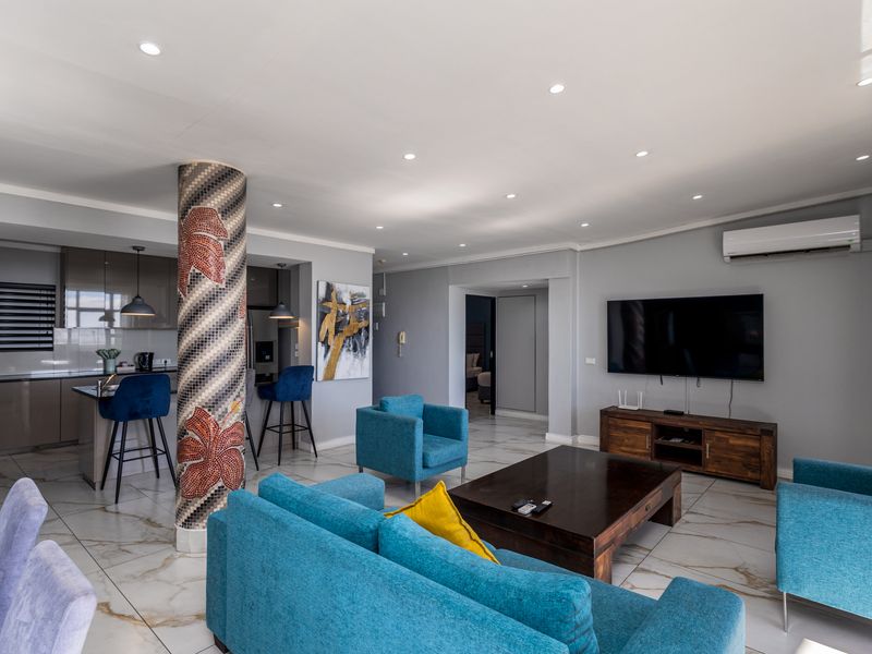 Spacious open-plan living area featuring marble-look floor tiles, a decorative mosaic column, recessed lighting, and a modern kitchen with integrated cabinetry.