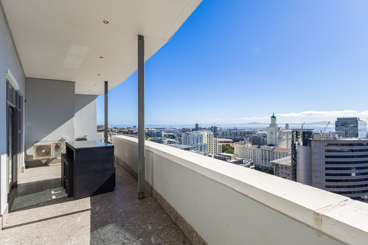 A spacious covered balcony featuring stone tile flooring, recessed lighting, and expansive city and ocean views.