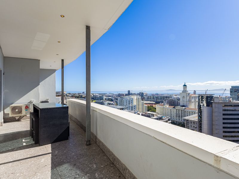 A spacious covered balcony featuring stone tile flooring, recessed lighting, and expansive city and ocean views.