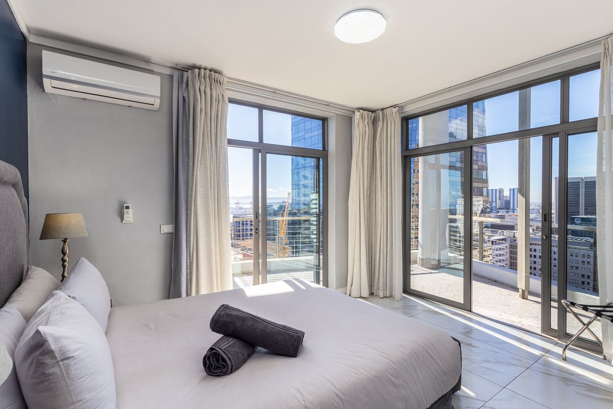 Modern bedroom featuring floor-to-ceiling glass sliding doors with direct balcony access, tiled flooring, and a wall-mounted air conditioning unit.