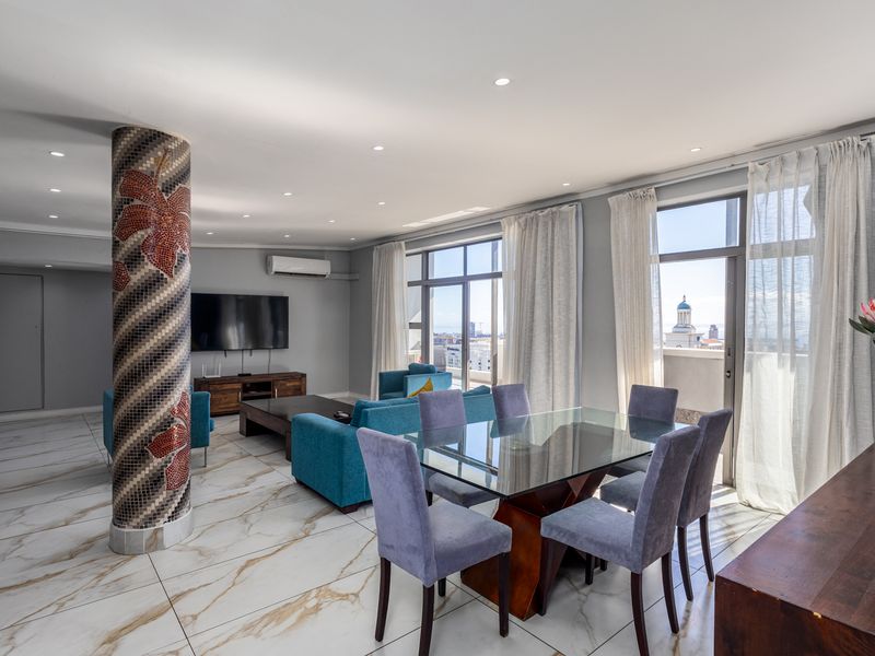 Spacious open-plan living and dining area featuring large format marble-look floor tiles, a decorative mosaic column, and direct access to a balcony with city views.