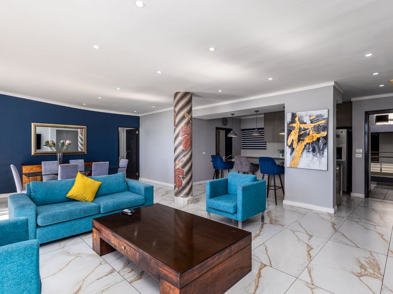 Spacious open-plan living and dining area featuring marble-look tiled flooring, recessed lighting, and a central decorative mosaic column.