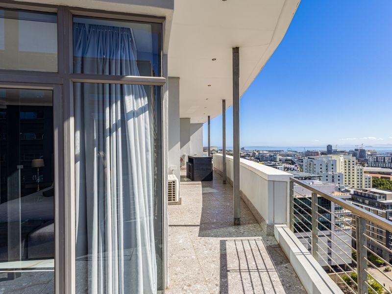 Spacious covered balcony featuring tiled flooring, metal railings, and expansive city views, accessible via large sliding glass doors.