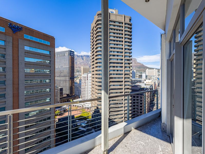 A private balcony featuring a metal balustrade and tiled flooring, offering expansive urban views of the city skyline and surrounding high-rise buildings.
