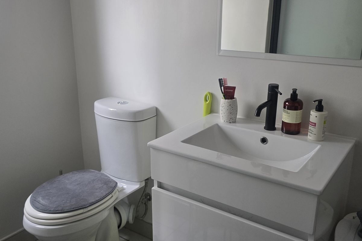 A modern bathroom featuring a white vanity with a black faucet, a wall-mounted mirror, and a standard toilet.