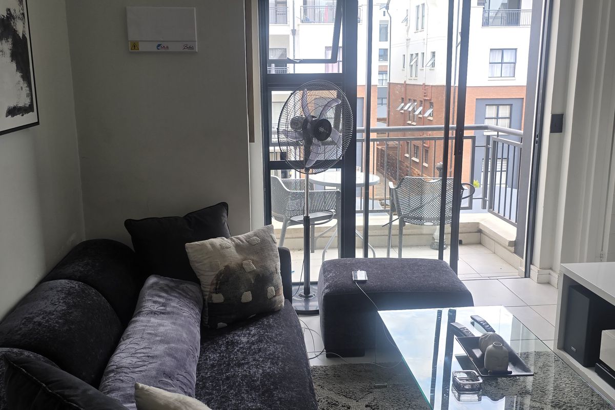 A compact living room featuring tiled flooring and large sliding glass doors that open onto a private balcony.