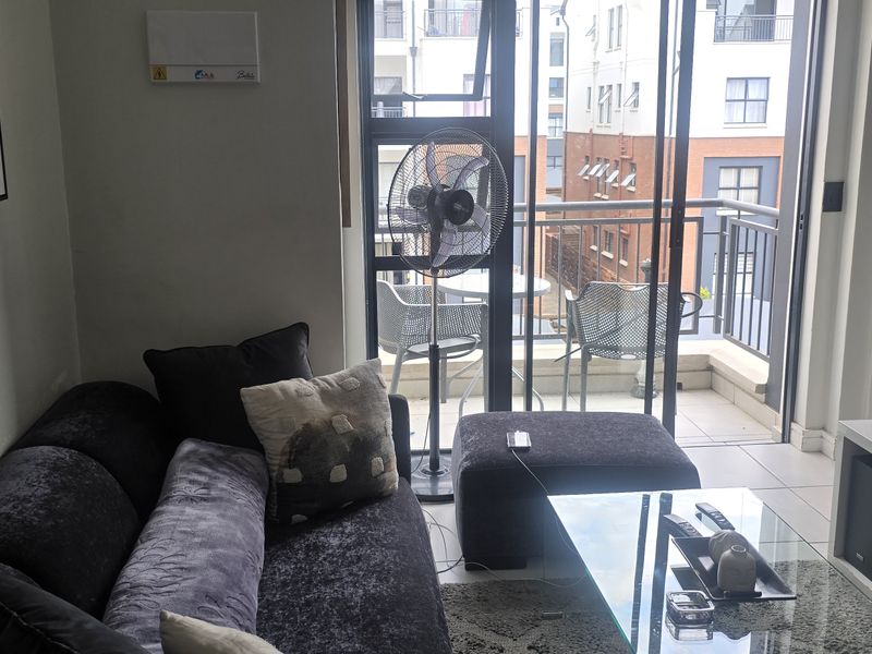 A compact living room featuring tiled flooring and large sliding glass doors that open onto a private balcony.