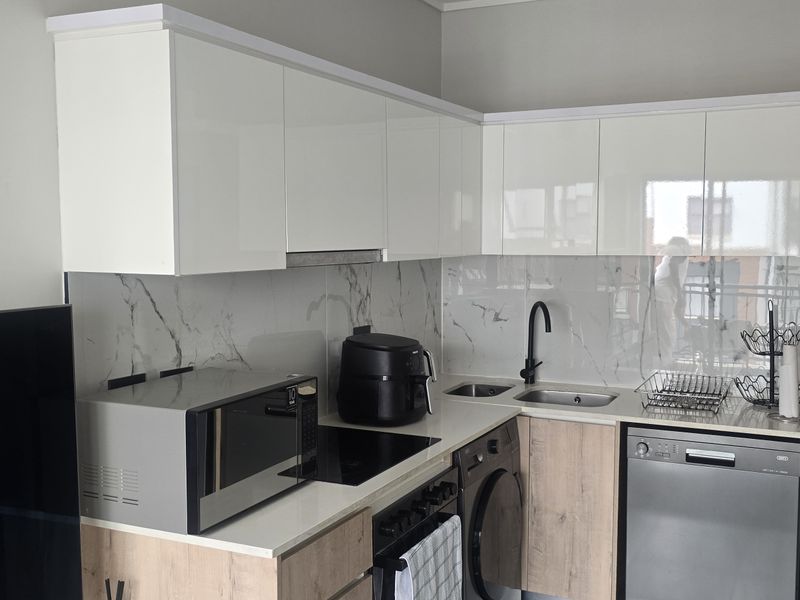 Modern kitchen featuring high-gloss white cabinetry, wood-grain lower cupboards, marble-look splashback, and integrated appliances including a hob and sink.