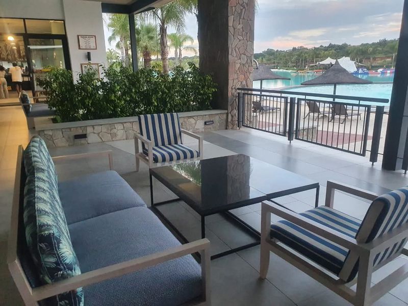 Covered patio area overlooking a swimming pool, featuring stone-clad pillars, tiled flooring, and metal railings.