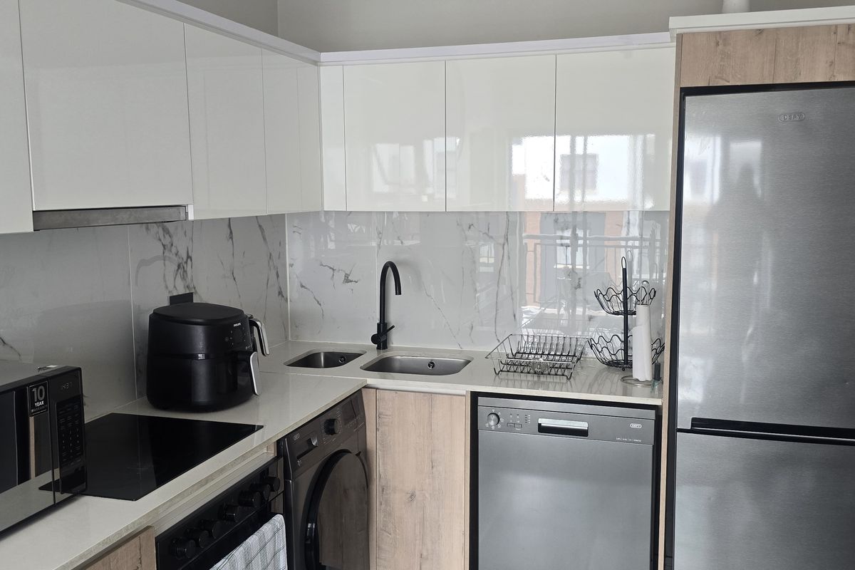 Modern kitchen featuring high-gloss white cabinetry, wood-grain accents, marble-look splashback, integrated sink, and built-in appliances.