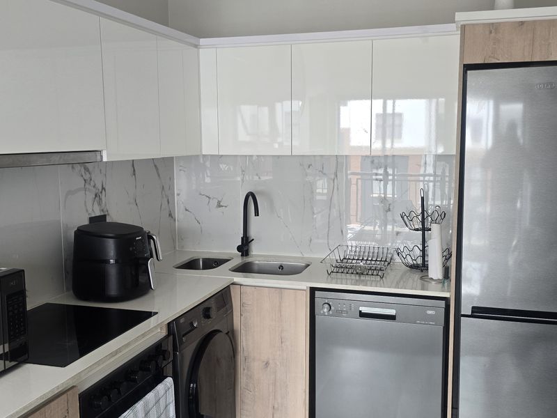 Modern kitchen featuring high-gloss white cabinetry, wood-grain accents, marble-look splashback, integrated sink, and built-in appliances.