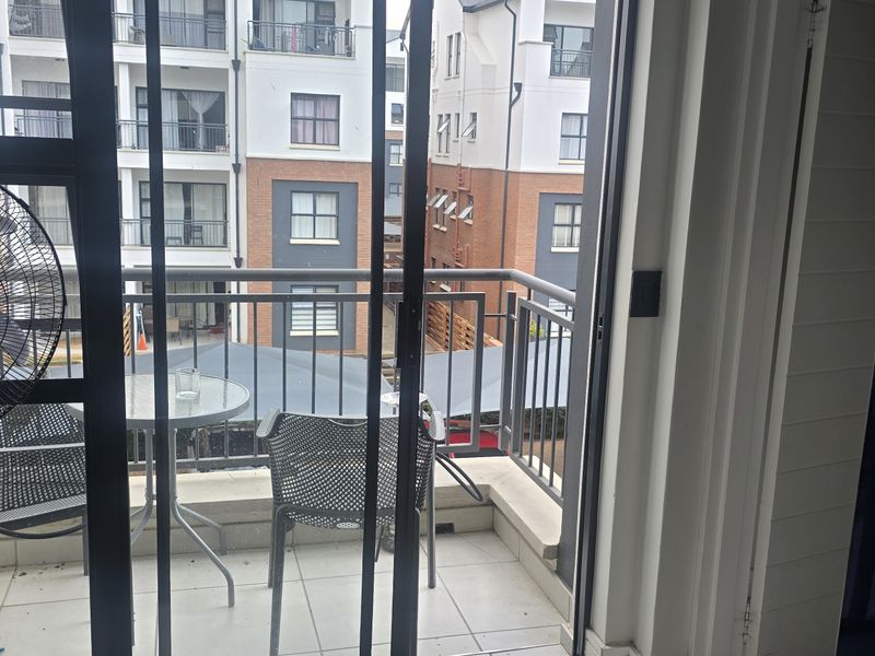 A view from an interior space looking out onto a tiled balcony with metal railings, overlooking a neighbouring apartment complex.