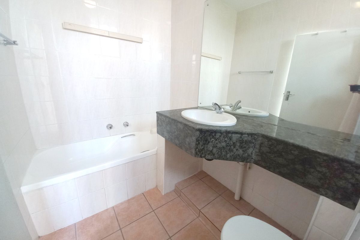 A functional bathroom featuring a built-in bathtub, a vanity with a stone countertop, and a large wall-mounted mirror.